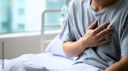 Man in hospital bed holding chest with hand indicating possible pain or heart issues in a room setting