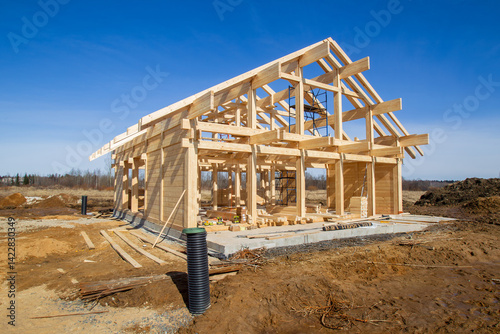 A wooden house frame under construction on a rural site with scattered materials and tools around. – Construction.