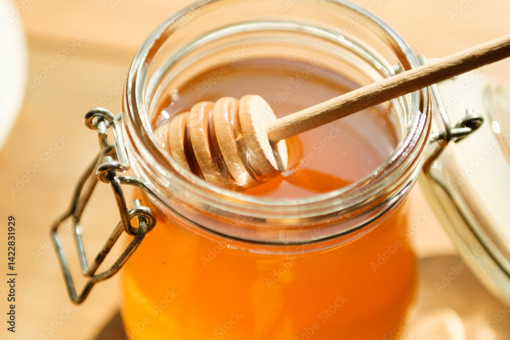 Golden honey fills a clear jar with a wooden dipper resting atop, illuminated by warm sunlight in a cozy setting perfect for culinary inspiration.