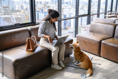 Businesswoman using laptop with her welsh corgi pembroke dog in modern coworking space