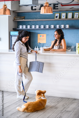 Woman is holding a portable pet bed and leash with her corgi in a pet friendly cafe, talking to the