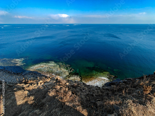 A breathtaking vista from a high coastal cliff showcases deep blue ocean waters meeting the horizon. the rocky coastline and clear skies add to the serene and expansive atmosphere of the scene