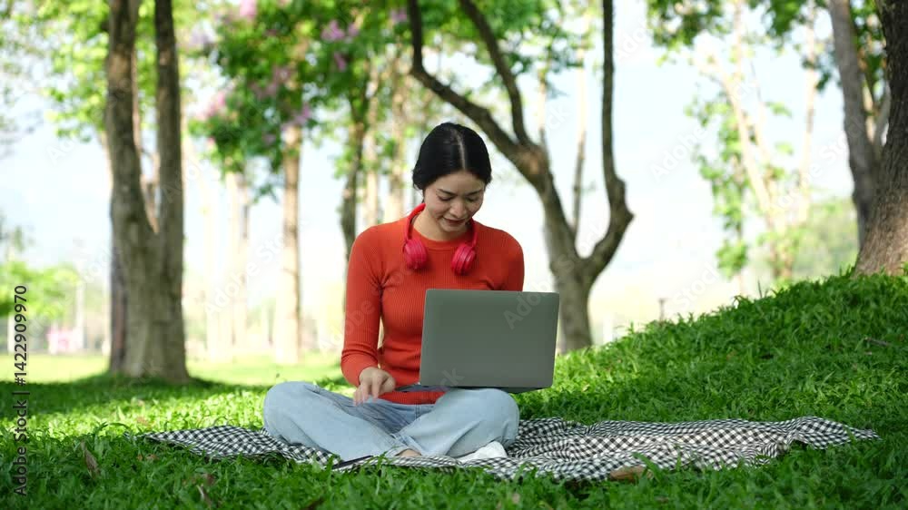 Asian woman sitting using laptop, working in a park Asian woman sitting using laptop, working in a park
