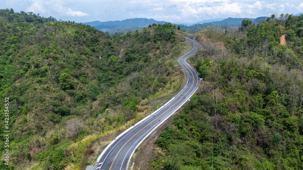 A winding road cuts through lush greenery, surrounded by hills and mountains under a bright blue sky, showcasing the beauty of nature and landscape. A winding road cuts through lush greenery, surrounded by hills and mountains under a bright blue sky, showcasing the beauty of nature and landscape.