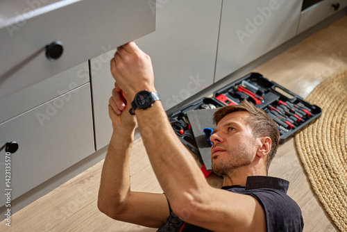 Obraz na płótnie Man assembling kitchen drawer in modern cabinet using screwdriver. Handyman installing and adjusting drawer slide mechanism in contemporary kitchen. Furniture installation w salonie