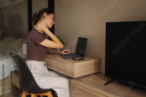 Tired girl working on laptop at table at home.
