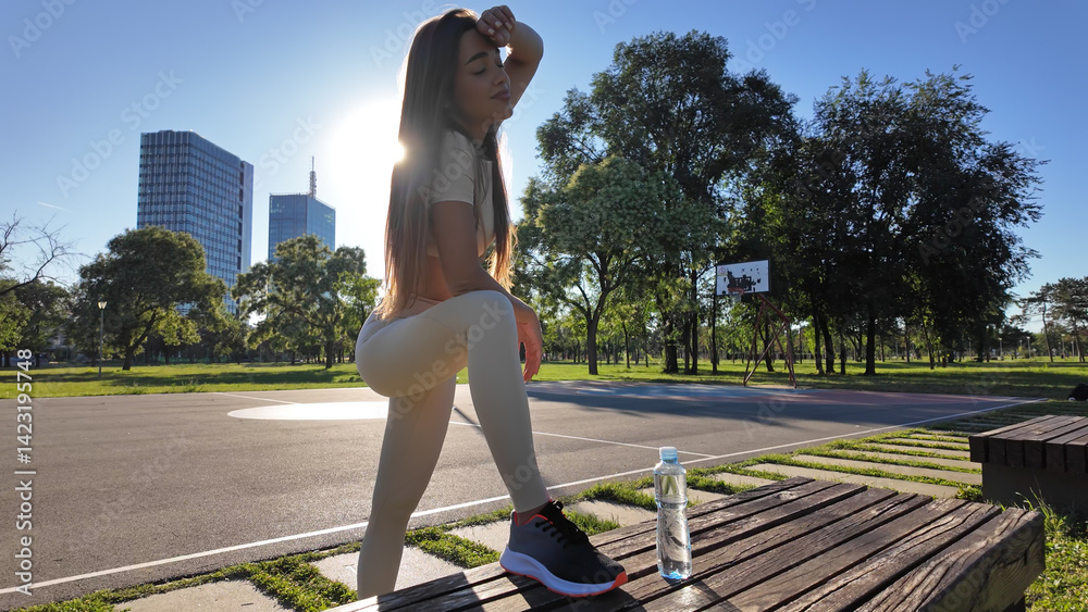 Young exhausted woman drinking water after jogging and exercise in urban park.