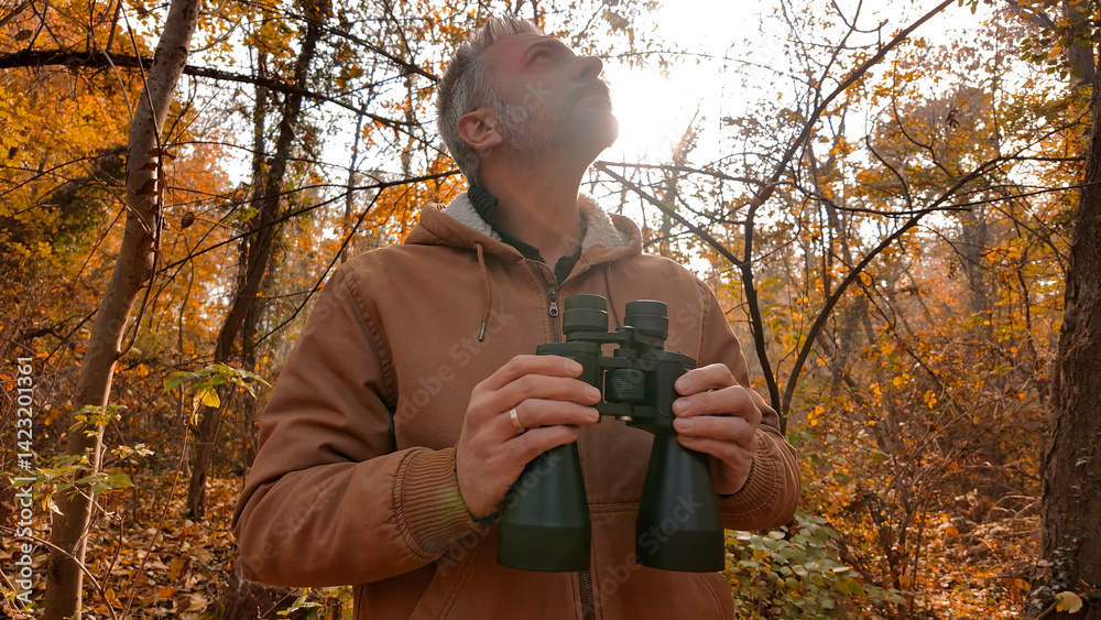 Amateur birdwatcher observing birds and other animals in nature with binoculars.