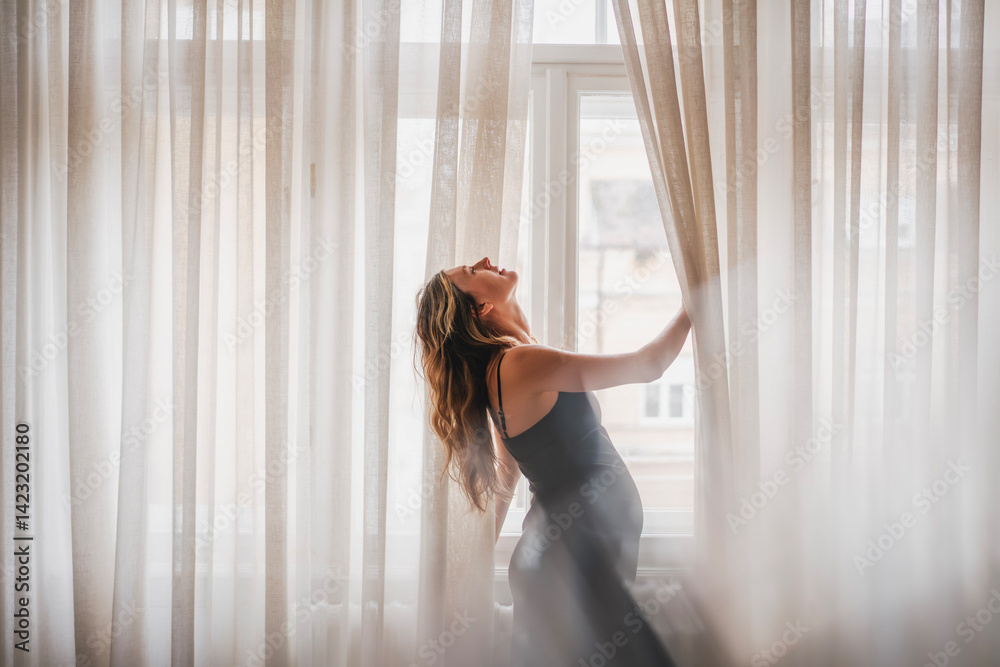 Portrait of young elegant caucasian pregnant woman in black slip dress standing by window