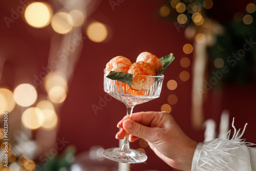 A woman's hand holds a cocktail glass with tangerines in it
