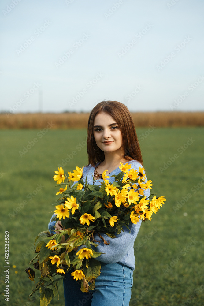 A woman in blue pants and a blue sweater holds a bouquet of yellow flowers in her hands A woman in blue pants and a blue sweater holds a bouquet of yellow flowers in her hands