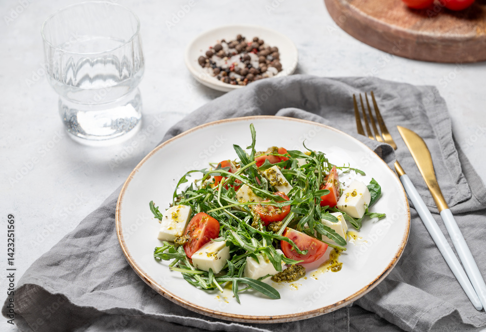 Healthy arugula salad with cherry tomatoes, mozzarella and pesto sauce on a plate Healthy arugula salad with cherry tomatoes, mozzarella and pesto sauce on a plate