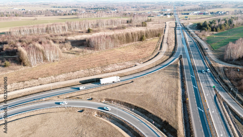 White semi-truck driving on a highway through countryside, aerial view from above showing the trucks shadow