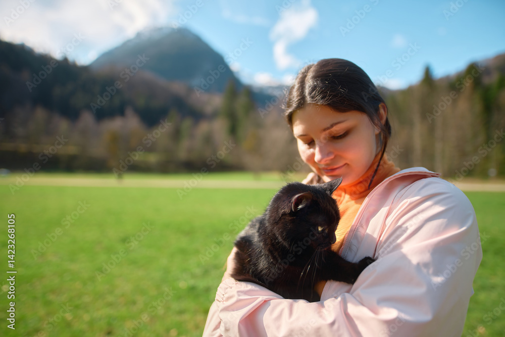 Woman embraces black cat in picturesque landscape
