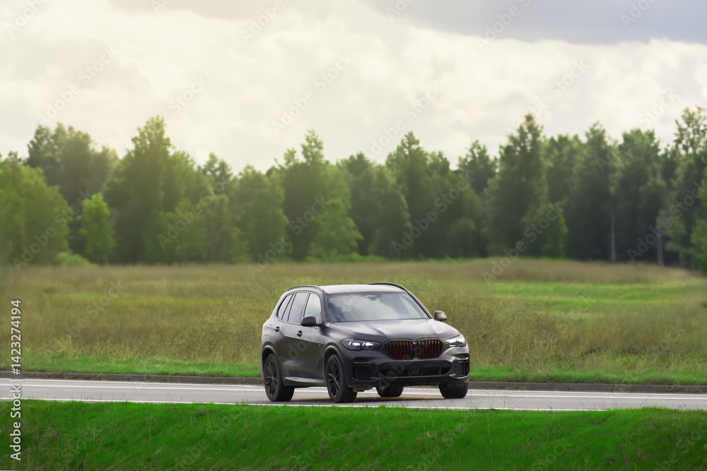 Expensive black SUV on a scenic road with lush green fields