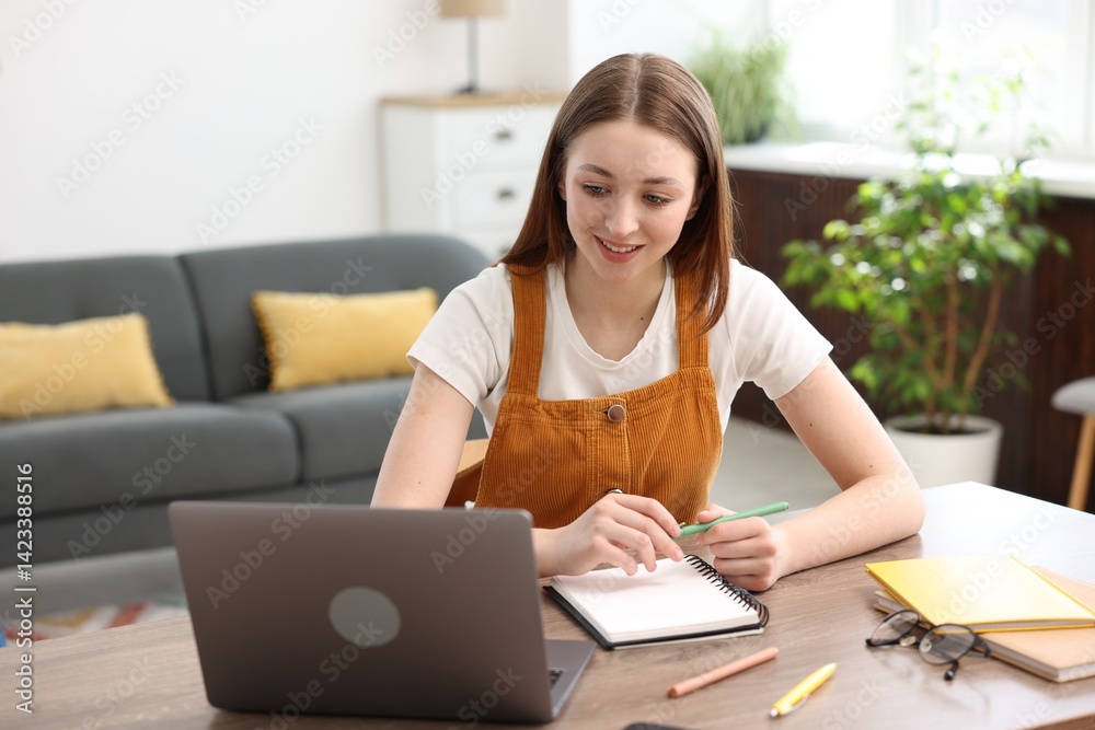 Teenage girl doing homework with laptop at table indoors Teenage girl doing homework with laptop at table indoors
