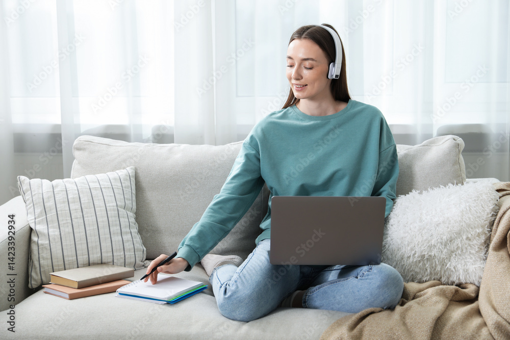 Naklejka premium Smiling woman taking notes during online lesson on sofa indoors. Self-study