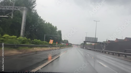 Car front view driving motorway M602 toward M60. Raining, slow short train on the left.