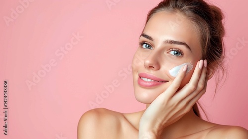 A woman applying cream, rubbing it into her skin, against a soft pastel pink background