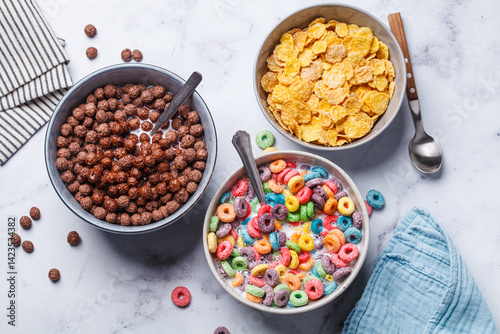 Different types of breakfast cereals background. Chocolate balls, cornflakes and colorful fruit rings on white background.
