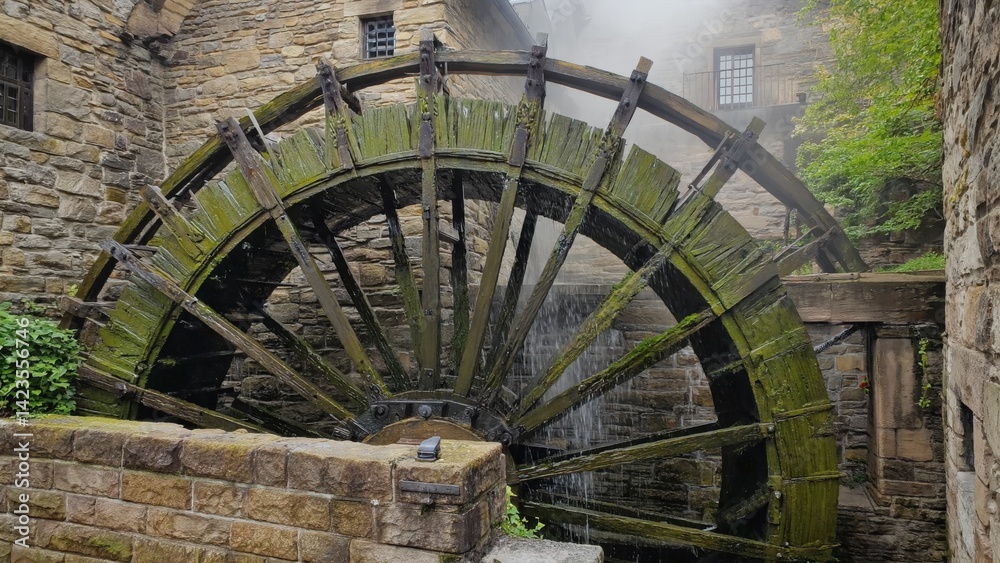 A large wooden water wheel attached to a stone mill building, showcasing historic machinery from an earlier time period.