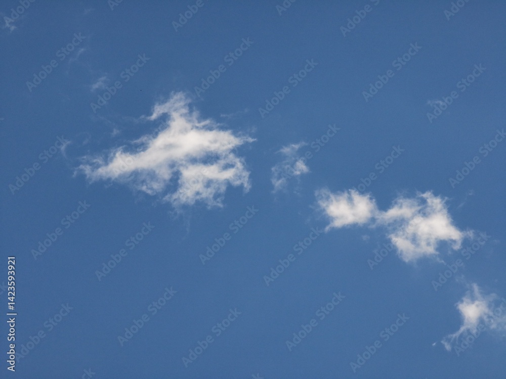 Two main wispy cloud clusters with trailing strands dispersed across a clear blue sky, forming a serene and minimal atmospheric background Two main wispy cloud clusters with trailing strands dispersed across a clear blue sky, forming a serene and minimal atmospheric background
