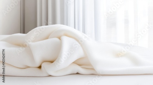 Soft, white draped fabric, likely a blanket, sits on a surface near a window