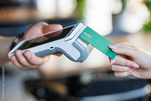 Woman making wireless payment with green card at electronic payment terminal.