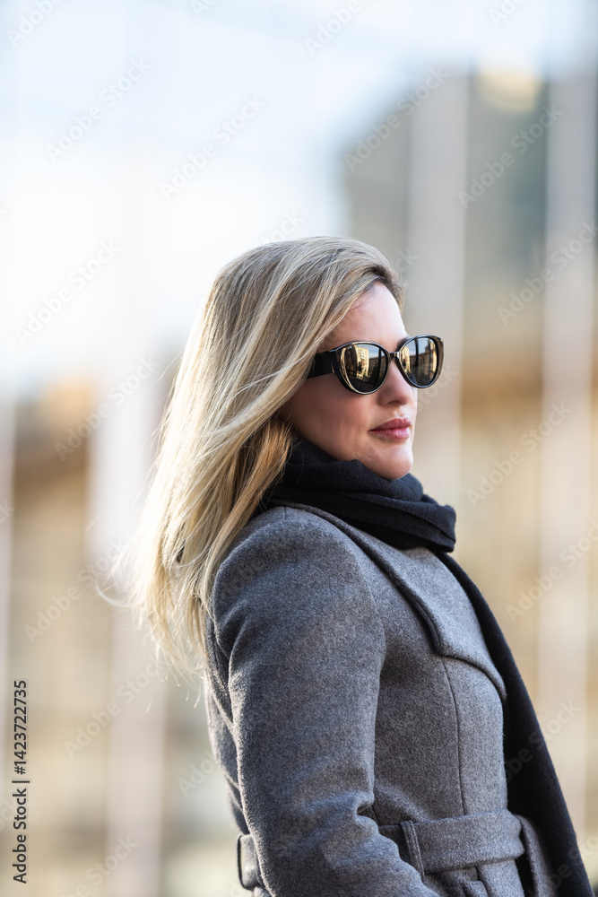Young beautiful blonde girl in coat with a black bag walks through the winter and spring city