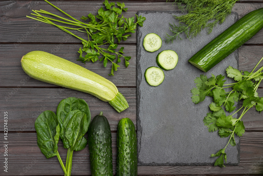 Sliced cucumber, cilantro and dill on cutting board. Zucchini, spinach and parsley on table