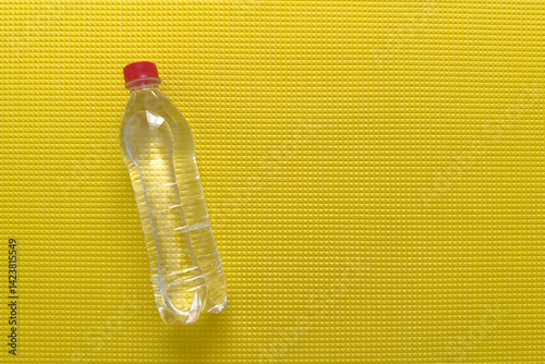 Fototapeta Naklejka Na Ścianę i Meble -  Plastic water bottle on bright yellow yoga mat with clear reflections in the morning light, space for text