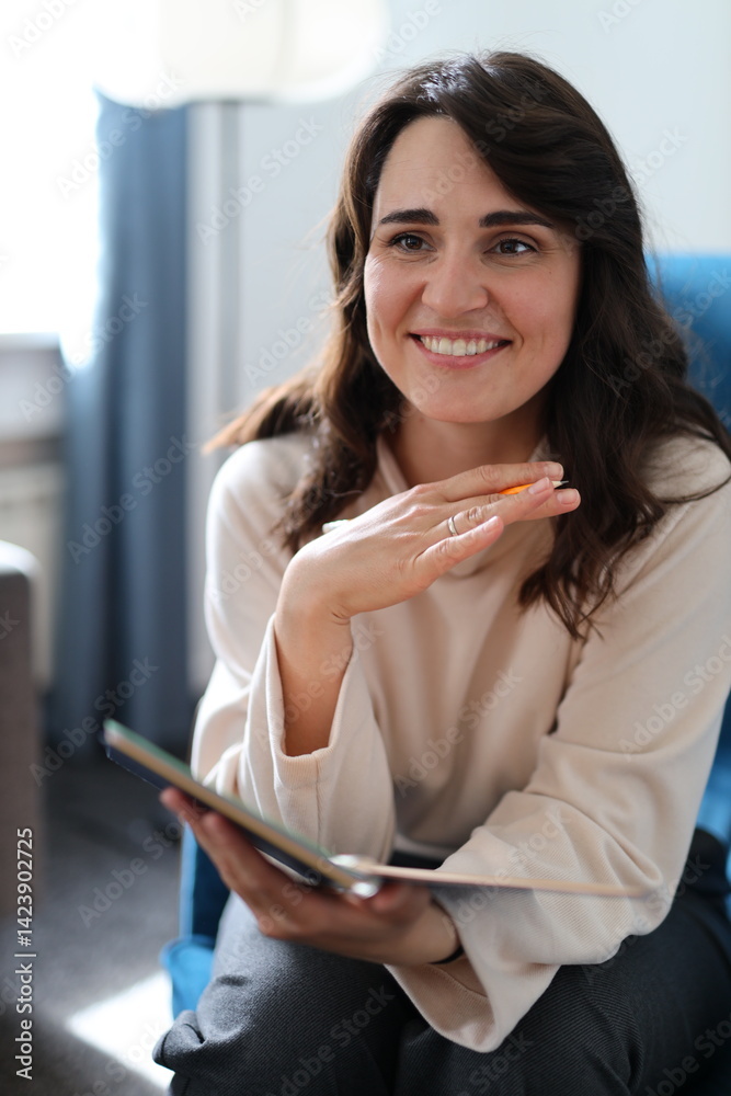 A woman is sitting on a chair with a book in her hand. She is smiling and she is happy A woman is sitting on a chair with a book in her hand. She is smiling and she is happy