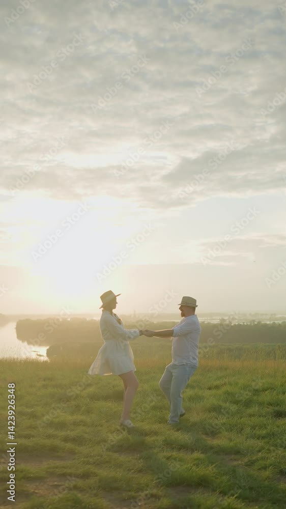 A loving couple spins joyfully on a grassy hill at sunset, beside a tranquil lake. The husband, in a white shirt and hat, embraces his wife in a flowing white dress, capturing a moment of love A loving couple spins joyfully on a grassy hill at sunset, beside a tranquil lake. The husband, in a white shirt and hat, embraces his wife in a flowing white dress, capturing a moment of love