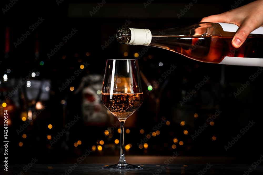 Fototapeta premium Rose pink wine glass and bottle in bartender hand on the black bar background with bokeh lights