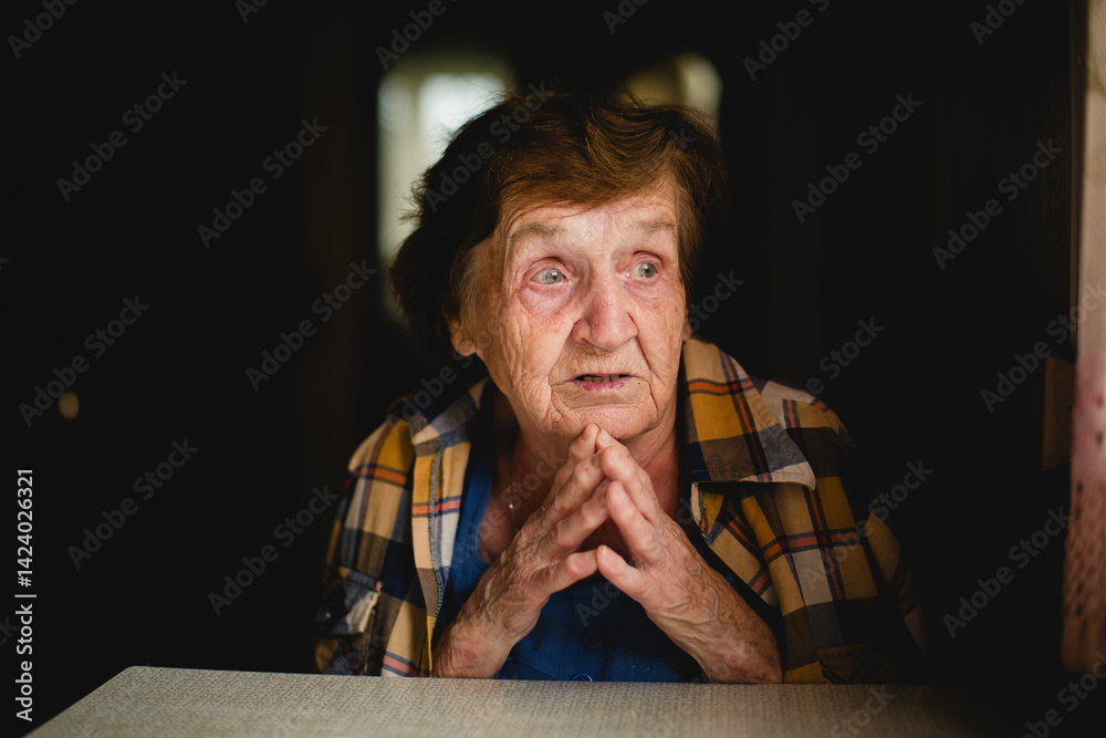 A portrait of an elderly woman with deeply emotional expression, her hands gently clasped, capturing a moment of quiet strength and vulnerability.