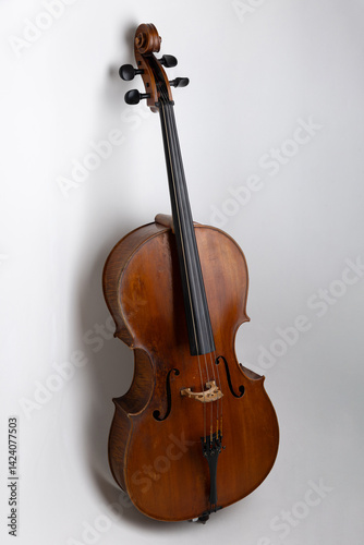 High-resolution studio photograph of a full-size classical cello standing vertically on a clean white background. The image showcases the elegant shape and wooden texture of the string instrument, com