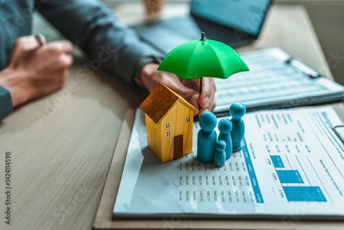 A wooden doll and wood house under an umbrella holding by agent represent insurance . house Family , protection, life.