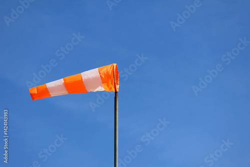 Orange and white striped wind sock against a blue sky. A conically shaped tube of woven textile used to indicate wind direction and speed. Aircraft wind indicator.