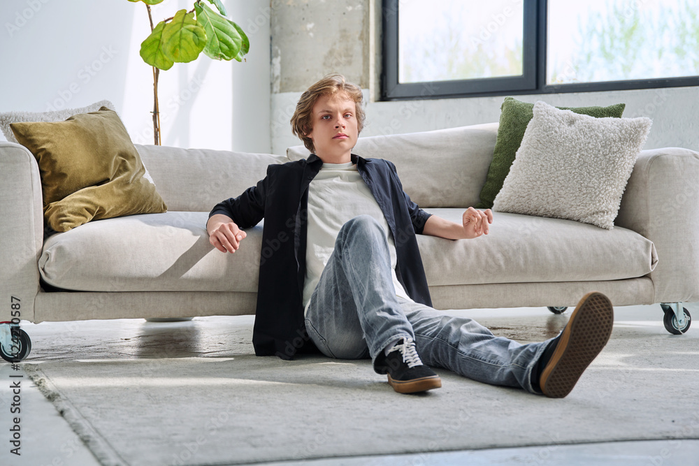 Portrait of handsome relaxed teenage boy sitting on floor near sofa in living room