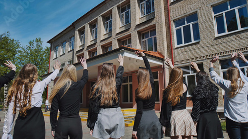 Obraz na płótnie Graduating high school girls waving farewell to their school building on their f