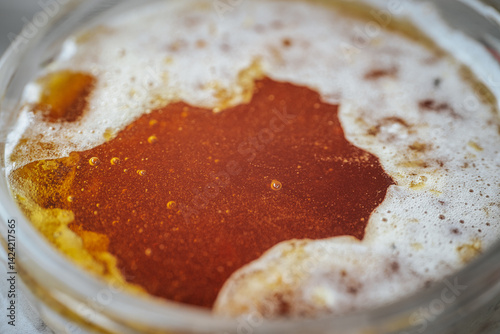  Close-up view of bubbly, fermenting honey in a glass jar on a rustic wooden surface. The frothy texture and amber color are prominent. Includes copy space.