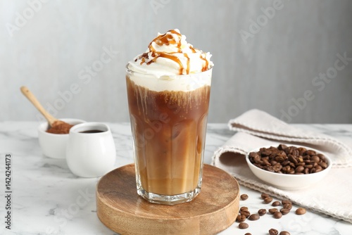 Tasty iced coffee with whipped cream, syrup and beans on white marble table