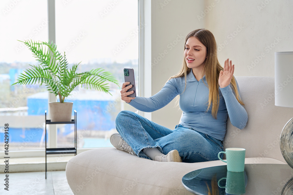 Young woman sitting at home in chair using smartphone, having video chat