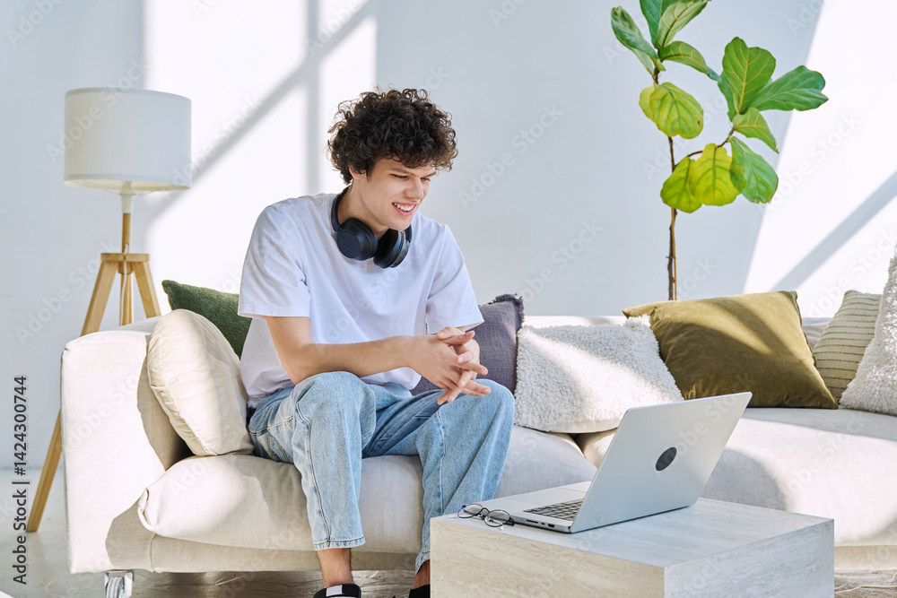 Young handsome smiling guy looking at laptop screen sitting on sofa at home