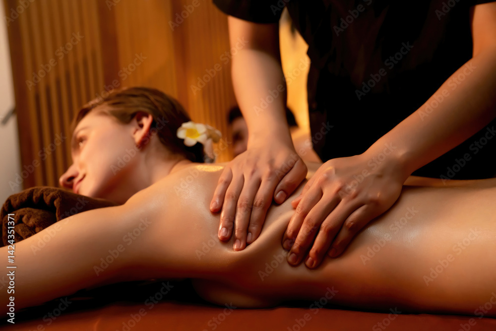 Fototapeta premium Caucasian couple customer enjoying relaxing anti-stress spa massage and pampering with beauty skin recreation leisure in warm candle lighting ambient salon spa at luxury resort or hotel. Quiescent