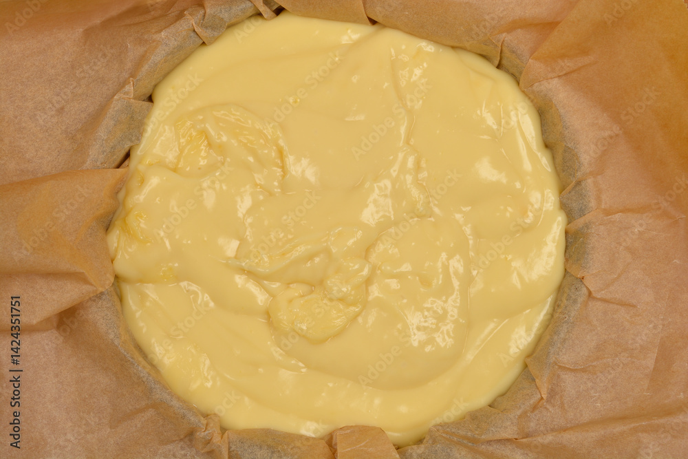 A top-down view of a light yellow vanilla and coconut cream cake filling set in a blue baking dish lined with parchment paper