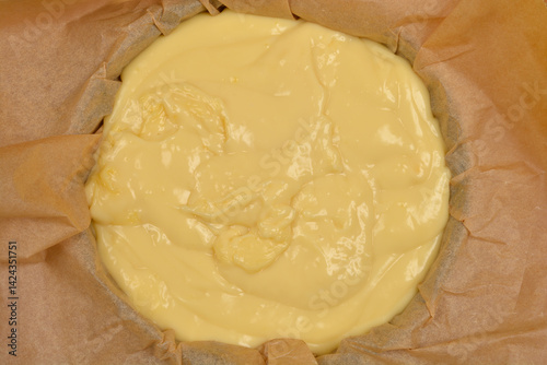 A top-down view of a light yellow vanilla and coconut cream cake filling set in a blue baking dish lined with parchment paper