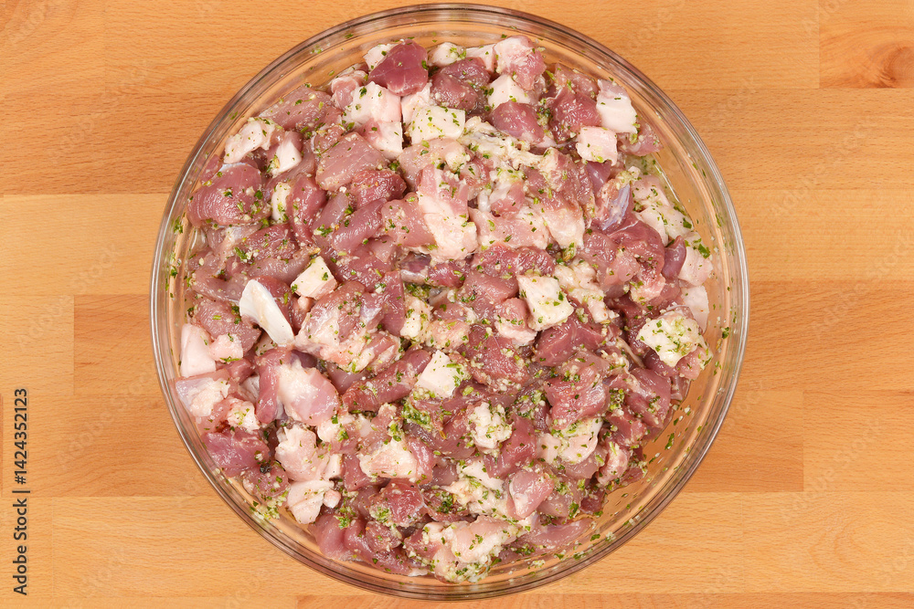 Diced and seasoned pork meat, ready for sausage making, is presented in a round glass bowl on a wooden background