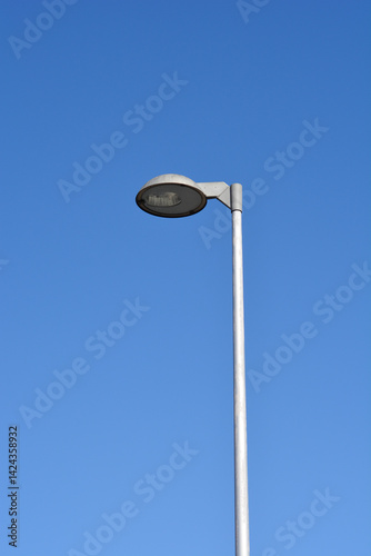 Obraz na płótnie A minimalist close-up photograph of a street lamp with a round shade, mounted on a metal pole, against a solid blue sky w salonie