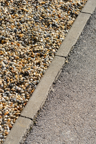 Obraz na płótnie A close-up shows a gray concrete curb separating a patch of small, multicolored gravel from an asphalt surface w salonie